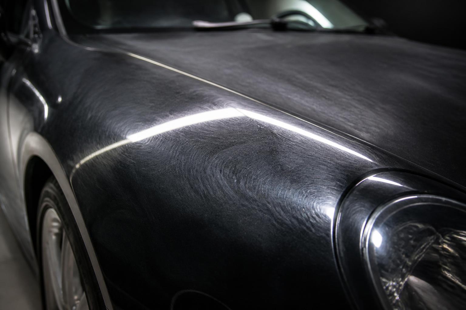 Black luxury car paint under inspection light with dense swirl marks and haze before correction